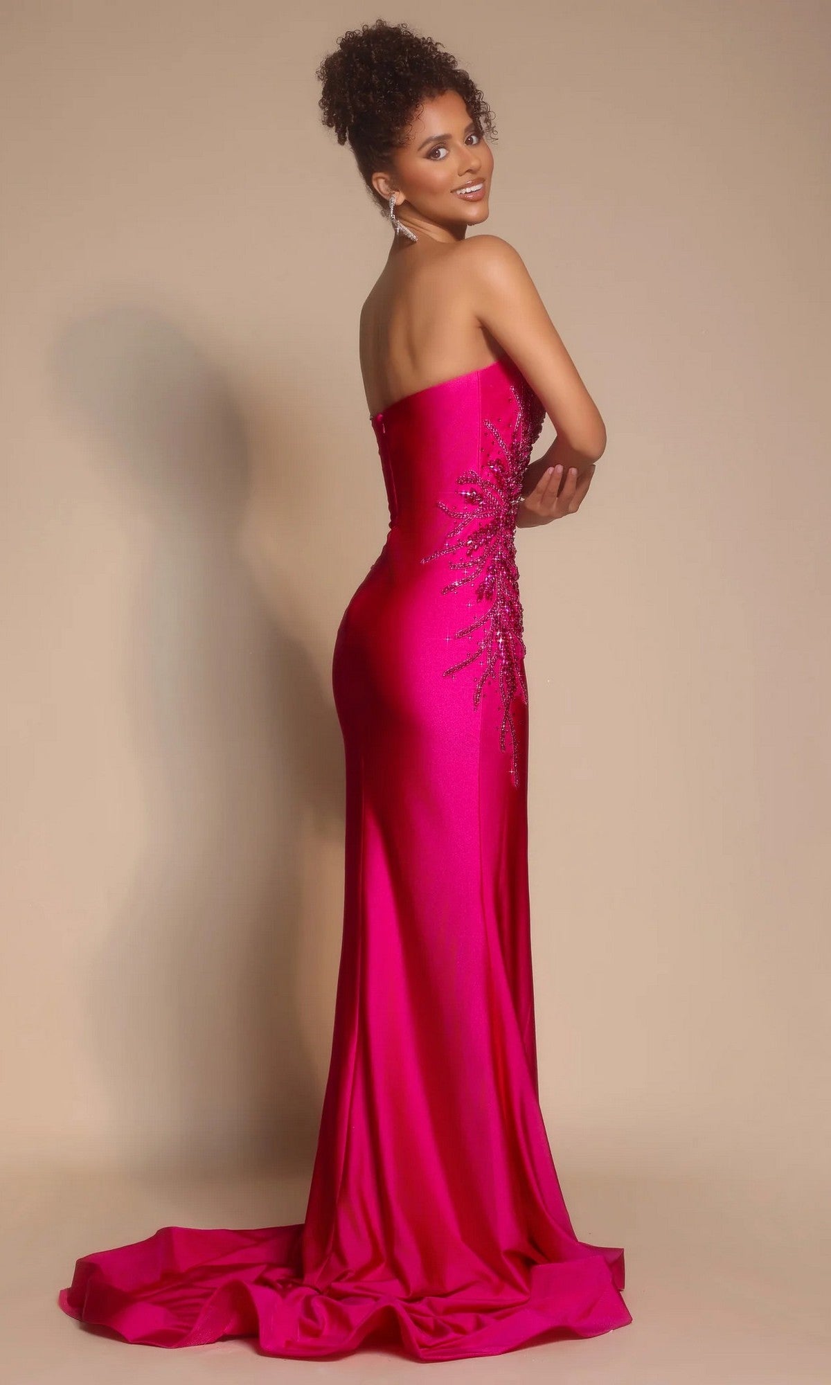 Woman in the Portia and Scarlett PS26331E long formal dress, featuring a strapless sweetheart neckline, floor-length hot pink design with side sequin detailing, poses against a beige background looking over her shoulder.